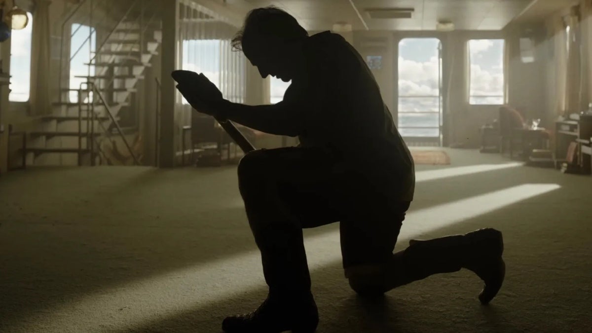 Tom Cruise kneeling with a shovel in a sunlit room in Digger (2026).